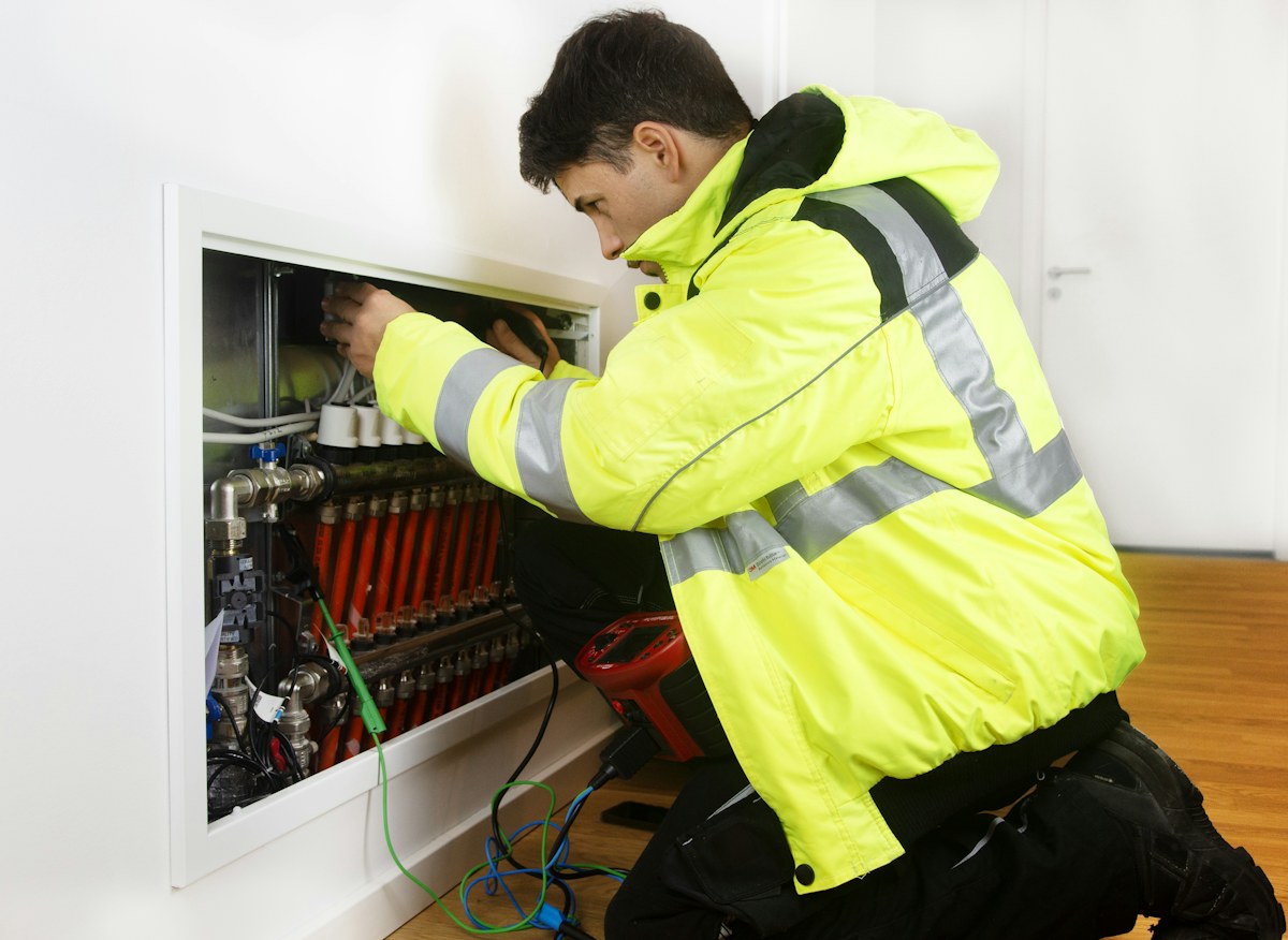 A technician in a hi-vis jacket working on a heating manifold