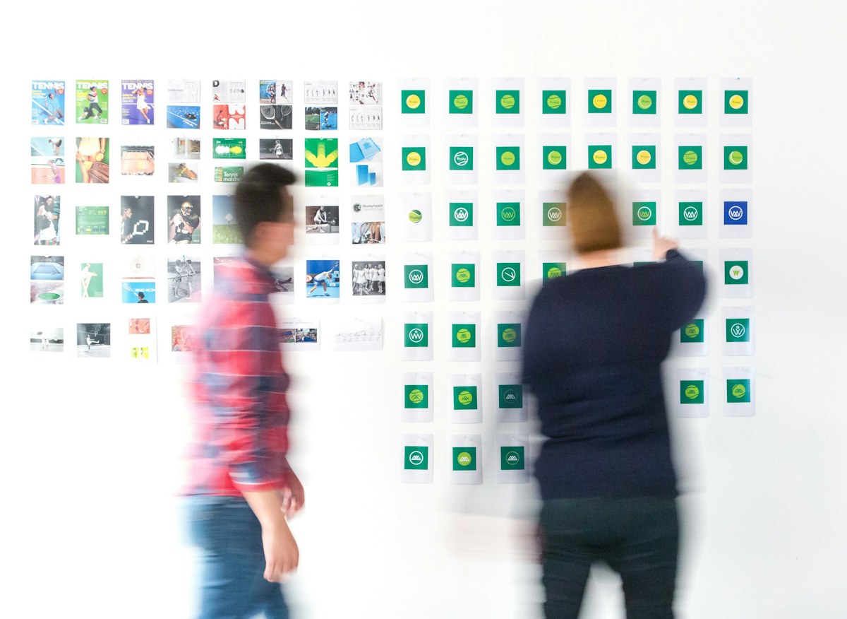 Two blurred people before a wall covered in small prints