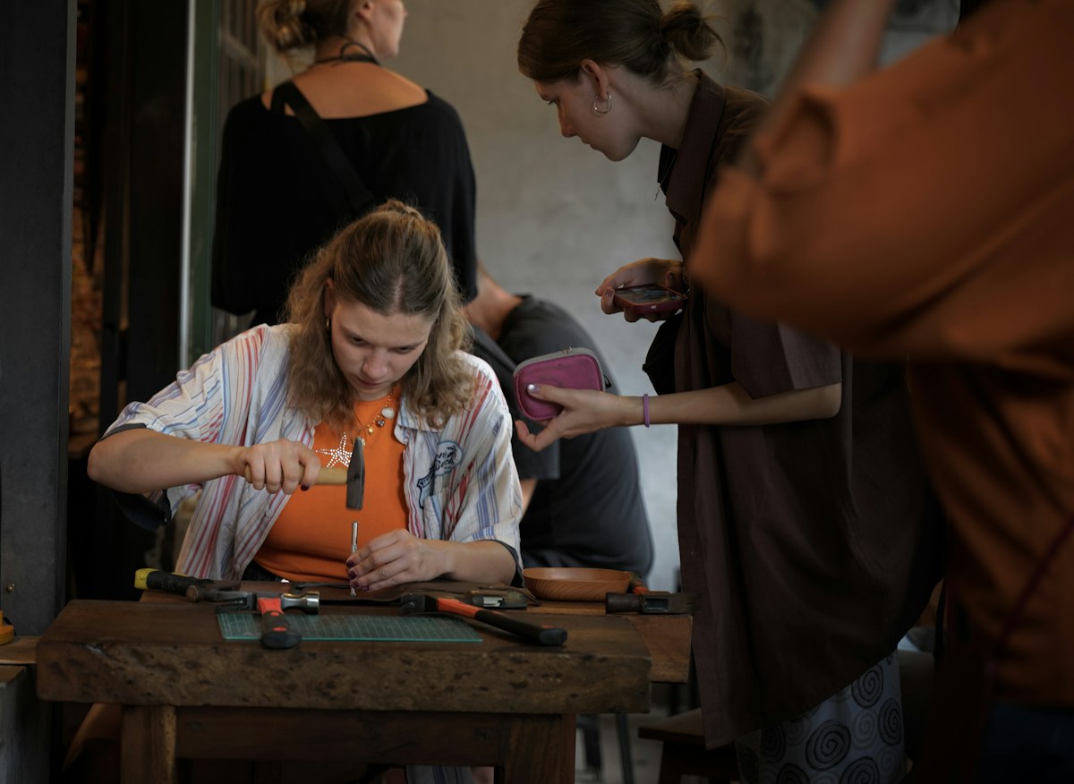 A maker hammering a tool into leather at a wooden workbench